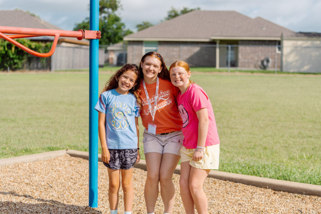 A Mentoring Alliance mentor smiling with two students on a school playground in Tyler, Texas